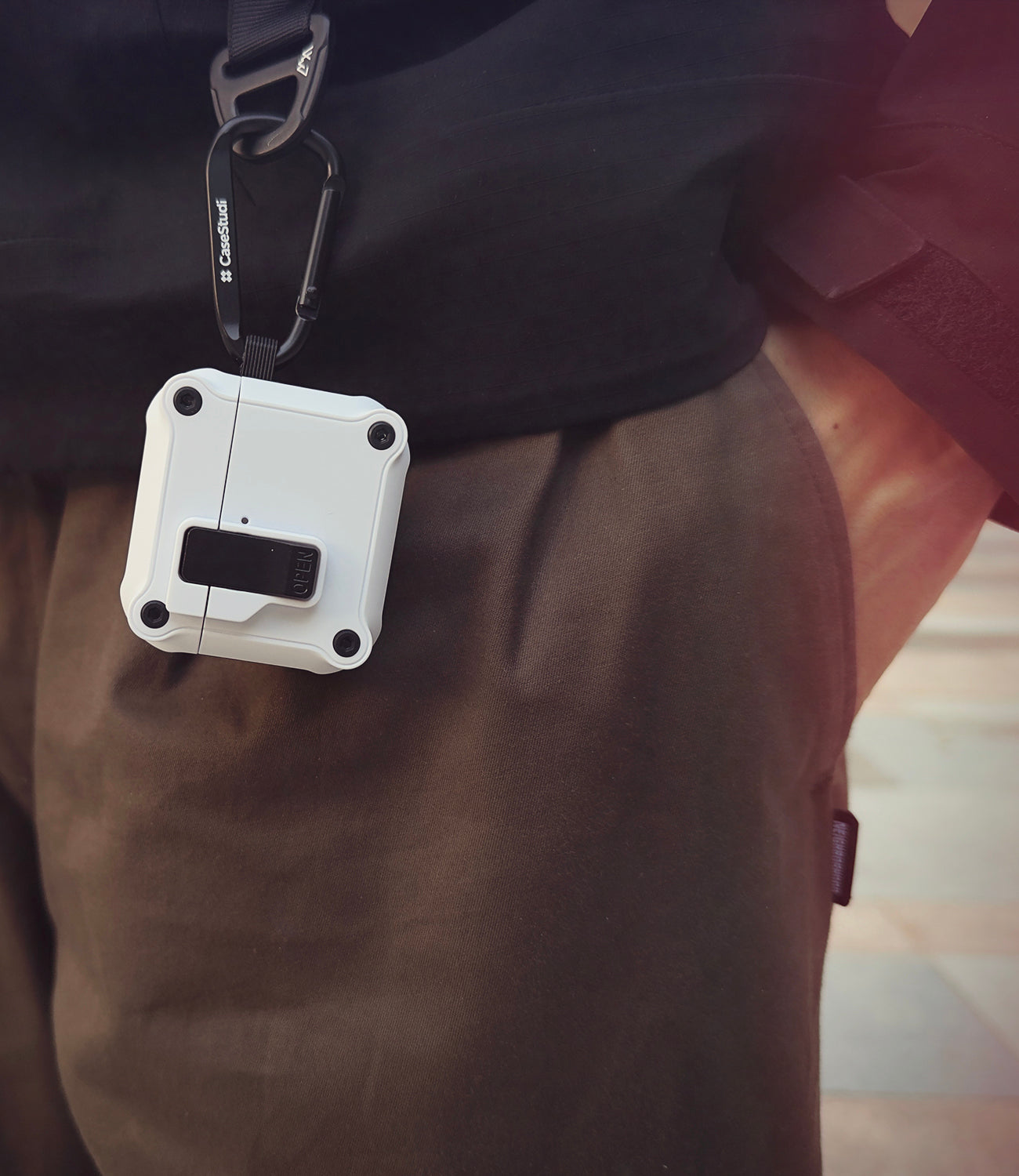 Casestudi white impact case for AirPods 4 with a carabiner, securely clipped to a sleek black Gore-Tex shell jacket. Engineered for ultimate protection with anti-drop durability and a magnetic lock, it’s perfect for keeping your earbuds safe during active days and outdoor adventures.