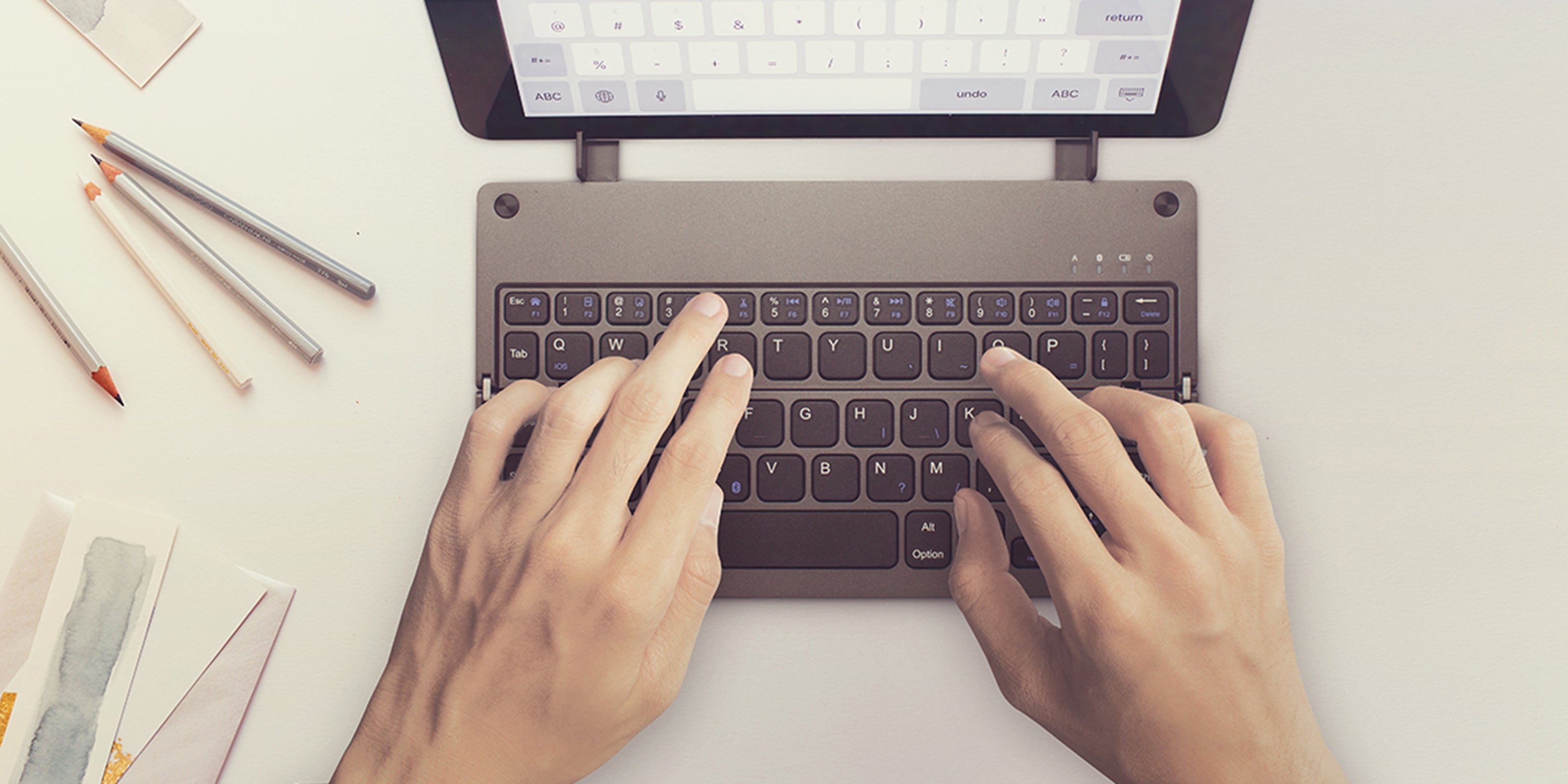 Casestudi Foldboard Stand in use, typing on an iPad, iPhone, and tablet, highlighting its versatility and functionality.