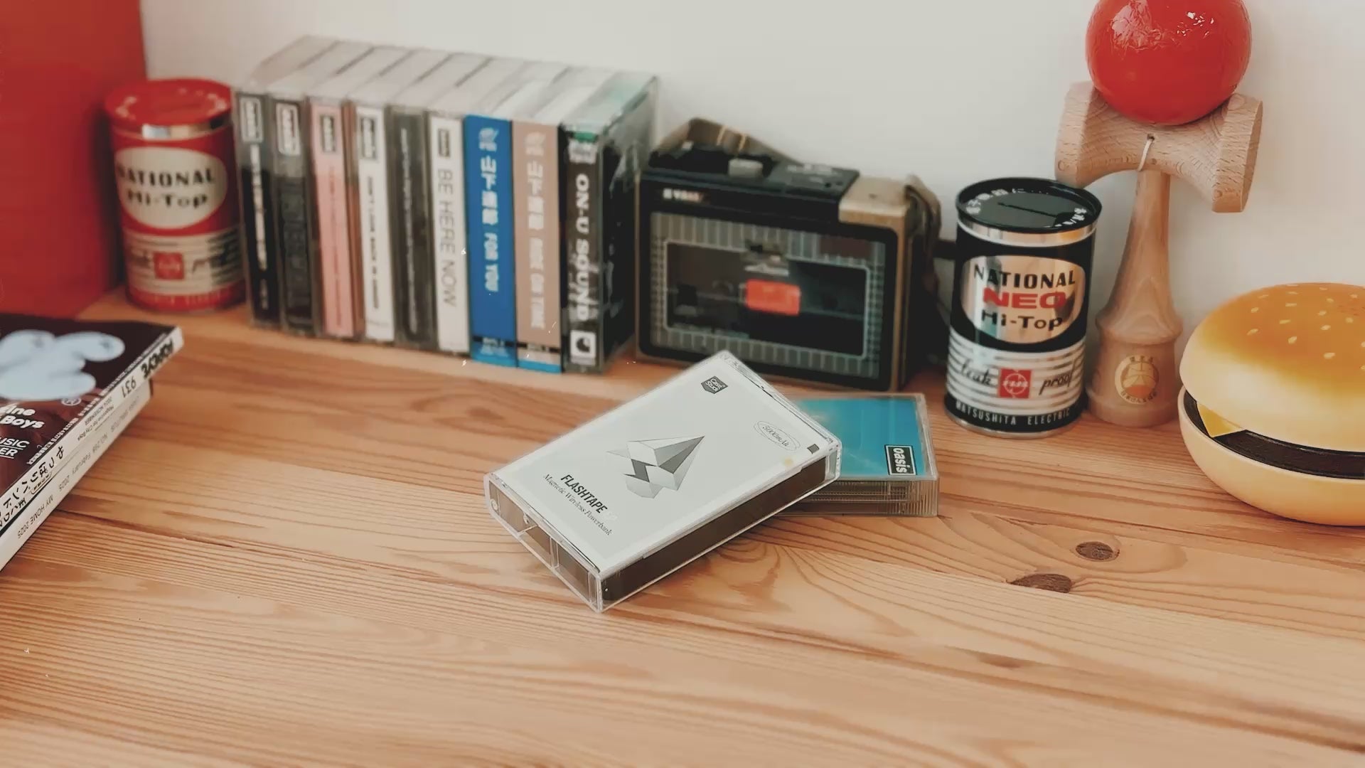 Casestudi Flashtape EP unboxing video set in a retro-inspired scene. The unboxing takes place on a wooden table with nostalgic items like Oasis cassettes, an 80s hamburger-shaped retro phone, and an old-school cassette player. The Flashtape EP comes in a real cassette box, revealing a cassette-shaped 5000mAh power bank. It includes stickers for customization, letting you write messages and relive the charm of the good old days.