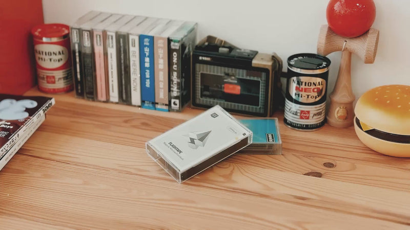 Casestudi Flashtape EP unboxing video set in a retro-inspired scene. The unboxing takes place on a wooden table with nostalgic items like Oasis cassettes, an 80s hamburger-shaped retro phone, and an old-school cassette player. The Flashtape EP comes in a real cassette box, revealing a cassette-shaped 5000mAh power bank. It includes stickers for customization, letting you write messages and relive the charm of the good old days.