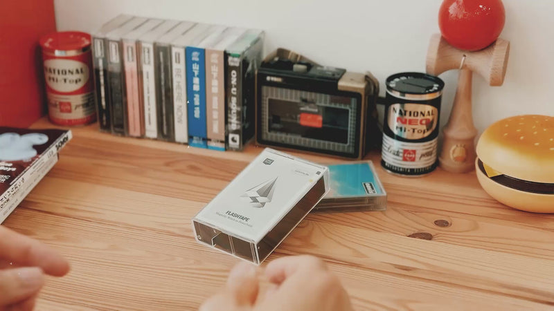 Casestudi Flashtape 10000mAh unboxing video set in a retro-inspired scene. The unboxing takes place on a wooden table with nostalgic items like Oasis cassettes, an 80s hamburger-shaped retro phone, and an old-school cassette player. The Flashtape 10000mAh comes in a real cassette box, revealing a cassette-shaped 10000mAh power bank. It includes stickers for customization, letting you write messages and relive the charm of the good old days.